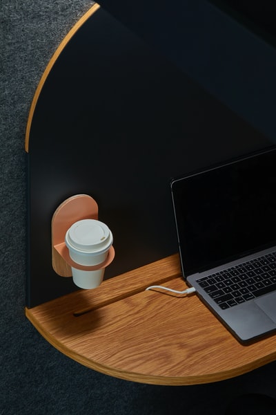 黑色笔记本电脑放在挂着白色杯子的棕色桌子上